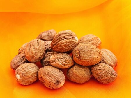 Heap of nutmegs over orange textile backgroundの写真素材