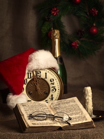 Christmas and New year theme with open Bible, vintage clock, candle, champagne, Santa`s hat and garland の写真素材
