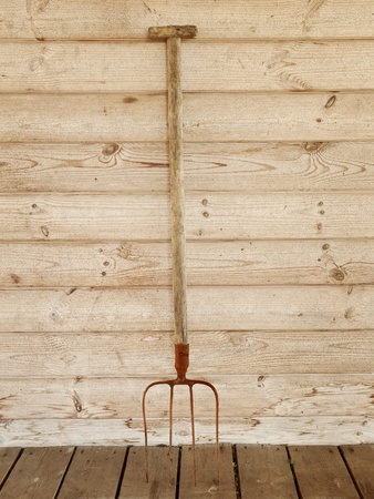 single rusty pitchfork near the wooden wallの写真素材