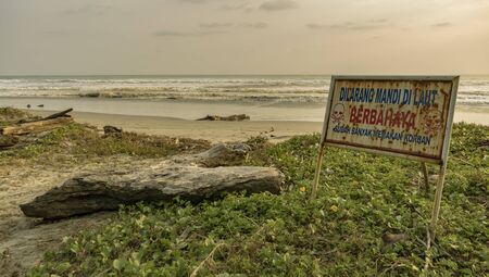 Warning sign in Indonesian language forbidding to swim in the ocean by wild beach because already many victims takenの写真素材