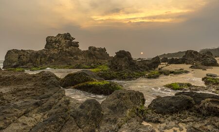 Dark sunset because of haze and clouds at pristine wild beach with no people around in Banten, Java, Indonesiaの写真素材
