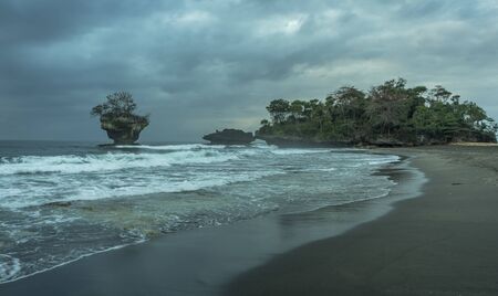 Amazing unique black sand beach location with rock islands off shore on a dark cloudy day in west Java, Indonesiaの写真素材