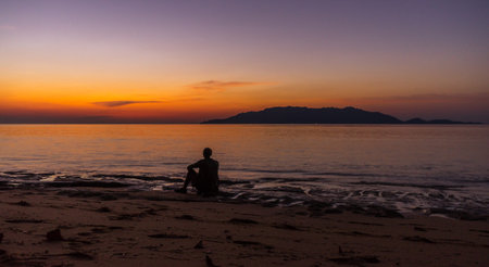Person sitting and enjoying evening sunset scene with Banda Besar island in distance very bright...
