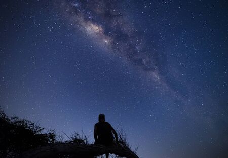 Person sitting on a tree branch at night enjoying milky way and sky full of stars dreamy moment at campsite in Sumbawaの写真素材