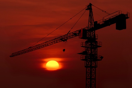 Industrial construction cranes and building silhouettes over sun at sunrise の写真素材