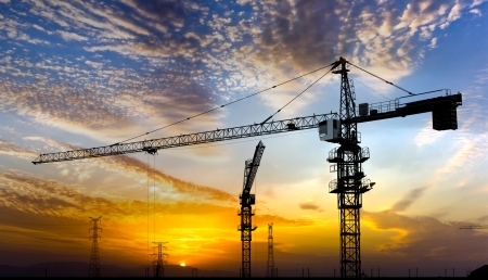 Industrial construction cranes and building silhouettes over sun at sunrise の写真素材