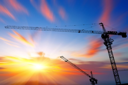 Industrial construction cranes and building silhouettes over sun at sunrise.のeditorial素材