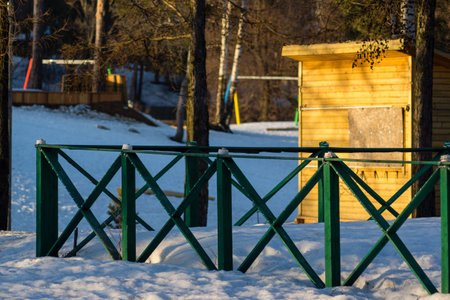 Green fence in winter snowdrifts and yellow wooden stallの写真素材