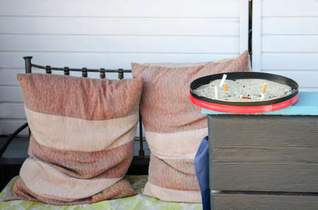 large ashtray with smoked cigarettes on the background of a sofa with pillows.の写真素材