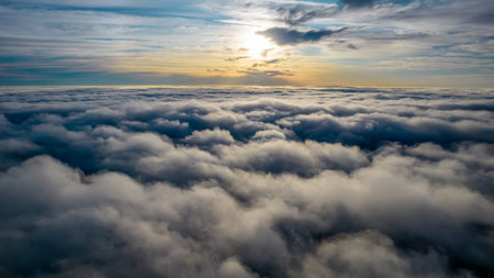 Aerial view of bright yellow sunset over white dense clouds with blue sky overhead.
