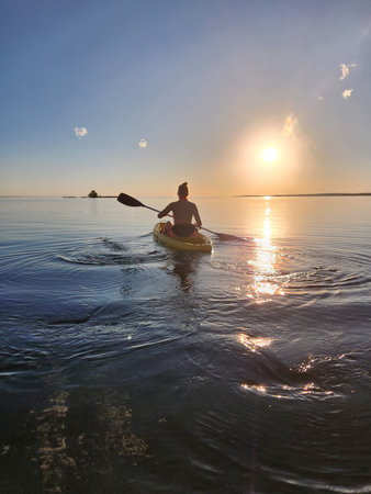 Women's silhouette rowing in kayak at sunset.の写真素材