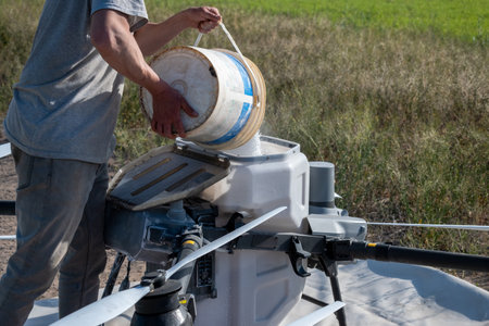 A farmer fills chemicals into the tank of a large agricultural drone to fertilize a planted field.の写真素材