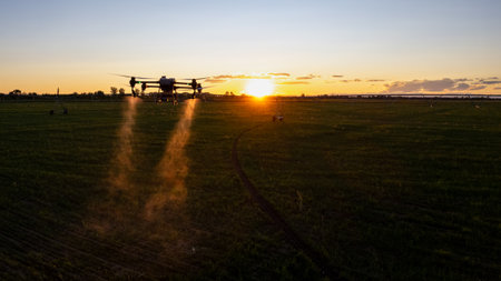 Agro drone works on the field. Field treatment with chemicals. Spraying pesticides against pests. Innovations in the agricultural sector. New technologies. Aerial. Sunsetの写真素材