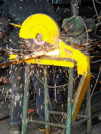 Close-up of a professional worker cutting metal profiles with an industrial grinder in a factory...