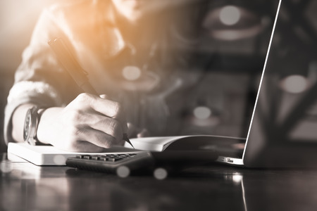 People writng on notebook and work with calculator and laptop on wooden tableの写真素材