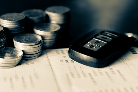 Row of coins on account book and car key remote in car finance conceptの写真素材