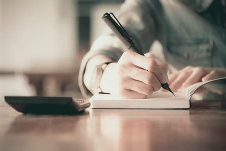 Close up women hand on writng on notebook and work with calculatorの写真素材