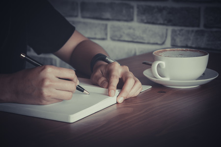 Close up of  people hand  writing on notebook on wooden tableの写真素材