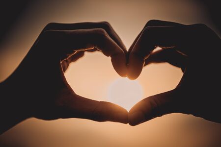 Close up of woman hand make heart shape in the sky at the sunsetの写真素材