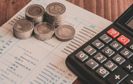 row of coins,calculator on the account book on the wooden table and black background in finance and banking conceptの写真素材