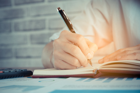 Close up of  people hand  writing on notebook on wooden tableの写真素材