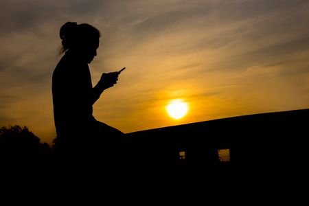 Side view of young girl using mobile phone in the sunset skyの写真素材