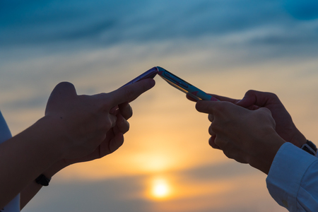 Close up side view of young women hand and her mobile phone in the sunset sky on communacation conceptの写真素材