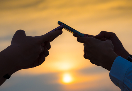 Close up side view of young women hand and her mobile phone in the sunset sky on communacation conceptの写真素材