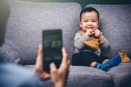 Happy young mother use smartphone or mobile phone take a photo to her son or child for memory.Family concept.の写真素材