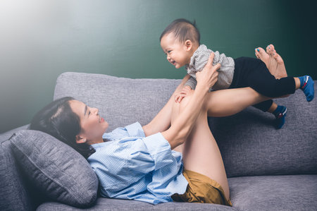 Happy young mother play with her son or child on sofa.Family concept.