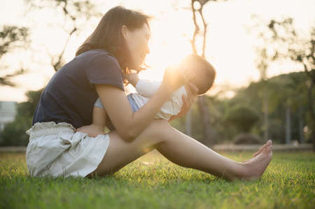 Young Asian mother playing with her son or cute baby on the ground in outdoor park.の写真素材