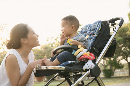 Young Asian mother playing with her son or cute baby on the ground in outdoor park.