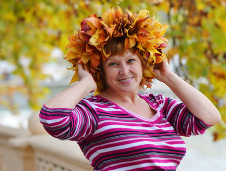 Portrait of a happy mature woman in a wreath of bright autumn leavesの写真素材