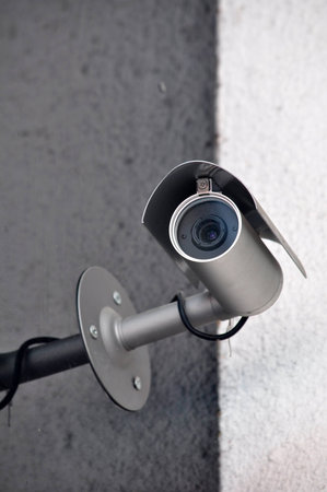 Black security camera in a cone on a gray wall 