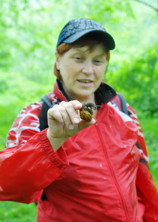 A woman catches a snail in the garden in spring (focus on the hand with a pest)