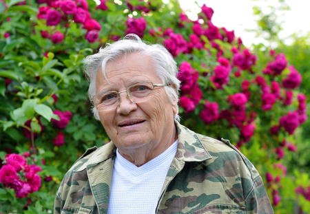 
Mature woman gardener looking thoughtfully into the camera on the background of blooming rosesの写真素材