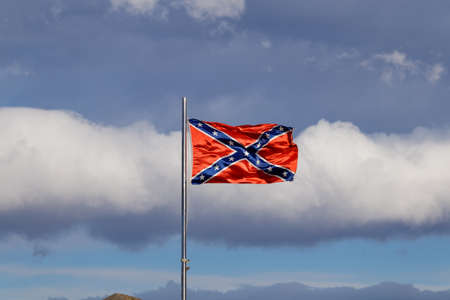 Confederate flag flutters on the wind against white cloudsの写真素材