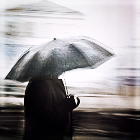 Man in a rain walking with umbrella. Unrecognizable person in motion blur.の写真素材