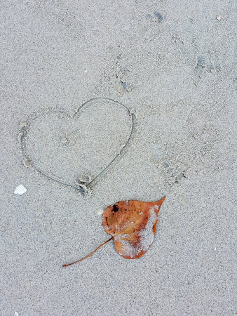 Dry leaves and hand written "heart "on sand beachの写真素材