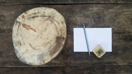 A white circle of wood was placed on a wooden table with a pencil and a blank white paper.