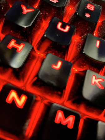 Close up of a computer keyboard with red glowing letters in it.