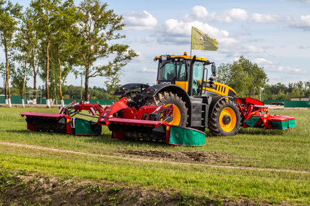 Russia, Leningrad Region - June, 2019: Agricultural work. Red tractor mowing the meadow. Farmer...