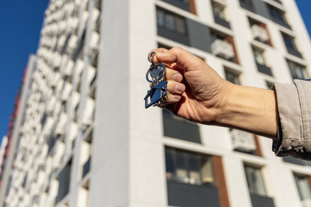 a mans hand holds the key to a new apartment on the background of a new buildingの写真素材