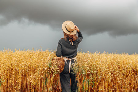 Girl in a wheat field wearing a straw hat on a cloudy day. Back view