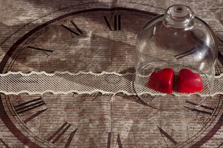 Red heart-shaped candy in a glass case on lace ribbon background of decorative old papeの写真素材