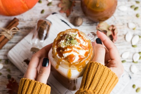 Spicy pumpkin latte with spices and a cap of whipped cream decorated with salted caramel and crushed pumpkin seedsの写真素材