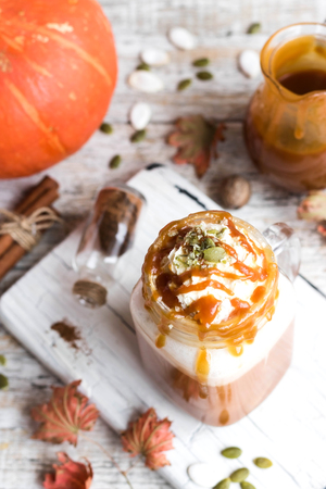Spicy pumpkin latte with spices and a cap of whipped cream decorated with salted caramel and crushed pumpkin seedsの写真素材