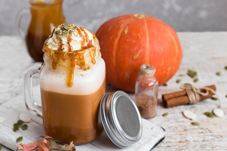Spicy pumpkin latte with spices and a cap of whipped cream decorated with salted caramel and crushed pumpkin seedsの写真素材