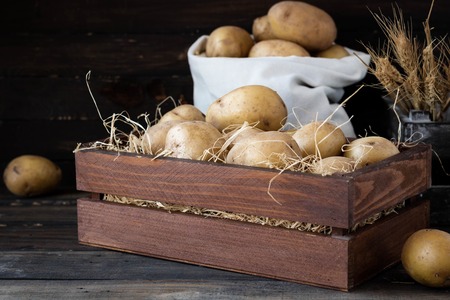 Organic raw potatoes in a wooden box in the straw on a dark backgroundの写真素材