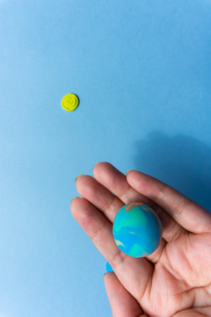 Woman holding plasticine model of planet Earth on blue background and sunの写真素材